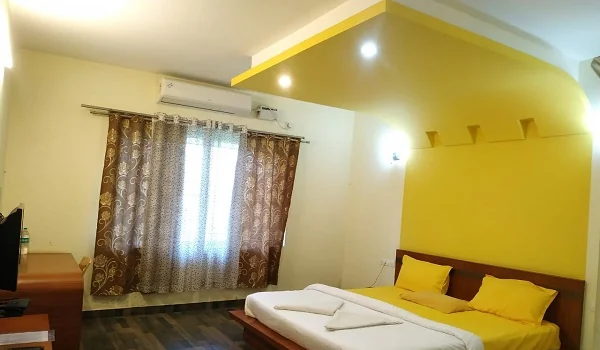 Deluxe air-conditioned room with yellow accent wall, TV and large window at Narasinha Mehta Dham
