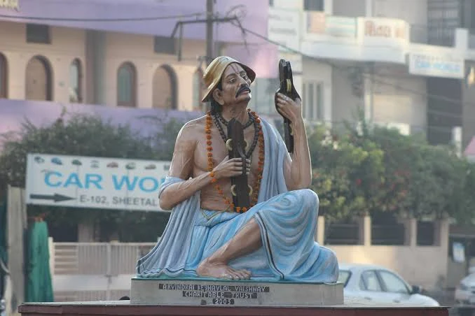 Statue of a seated devotional poet-saint with karatals and a marigold garland