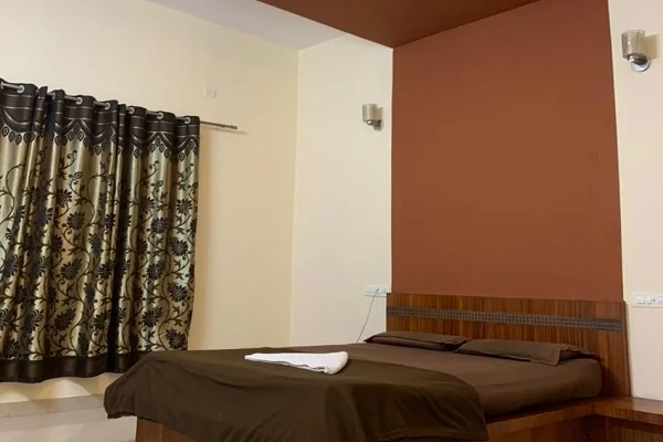 Standard double room with wooden bed, curtained window and warm accent wall at Narasinha Mehta Dham